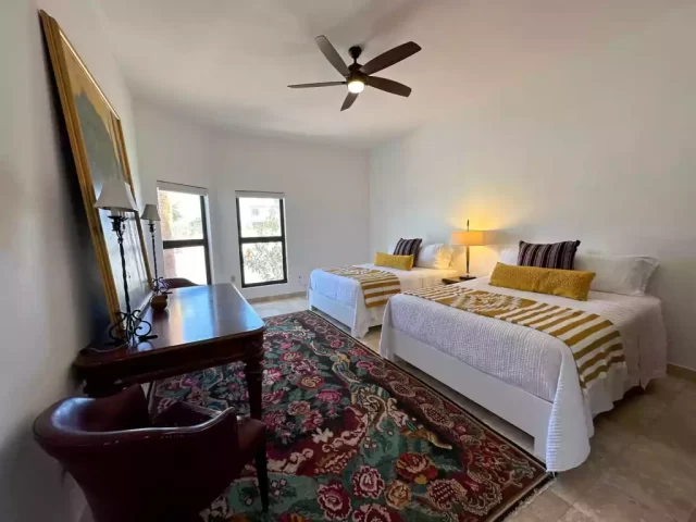 Two beds with yellow throws, colorful rug and wooden wardrobe in Casita 5